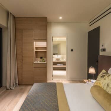 Side view of our Classic Room, showing the bed neatly made the wardrobe with water break area and open door leading to the bathroom.