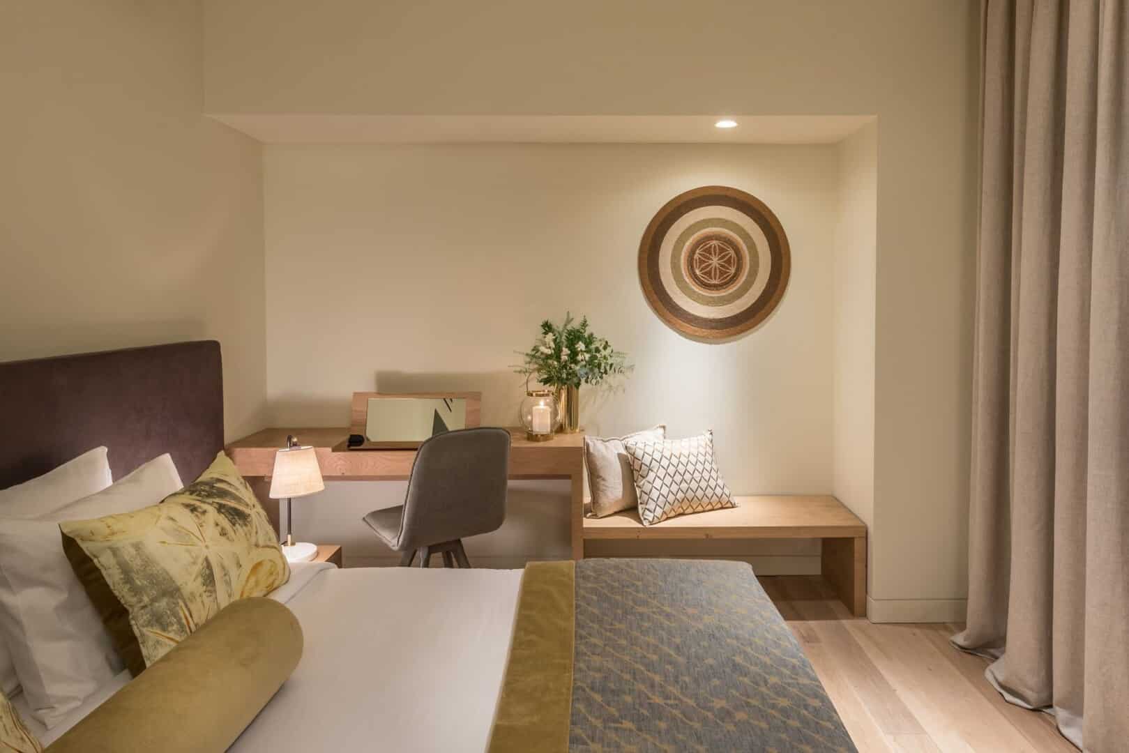 The interiors of our Classic Room, dressed in beige and earth tones, showing the bed and writing desk with bench beside it.