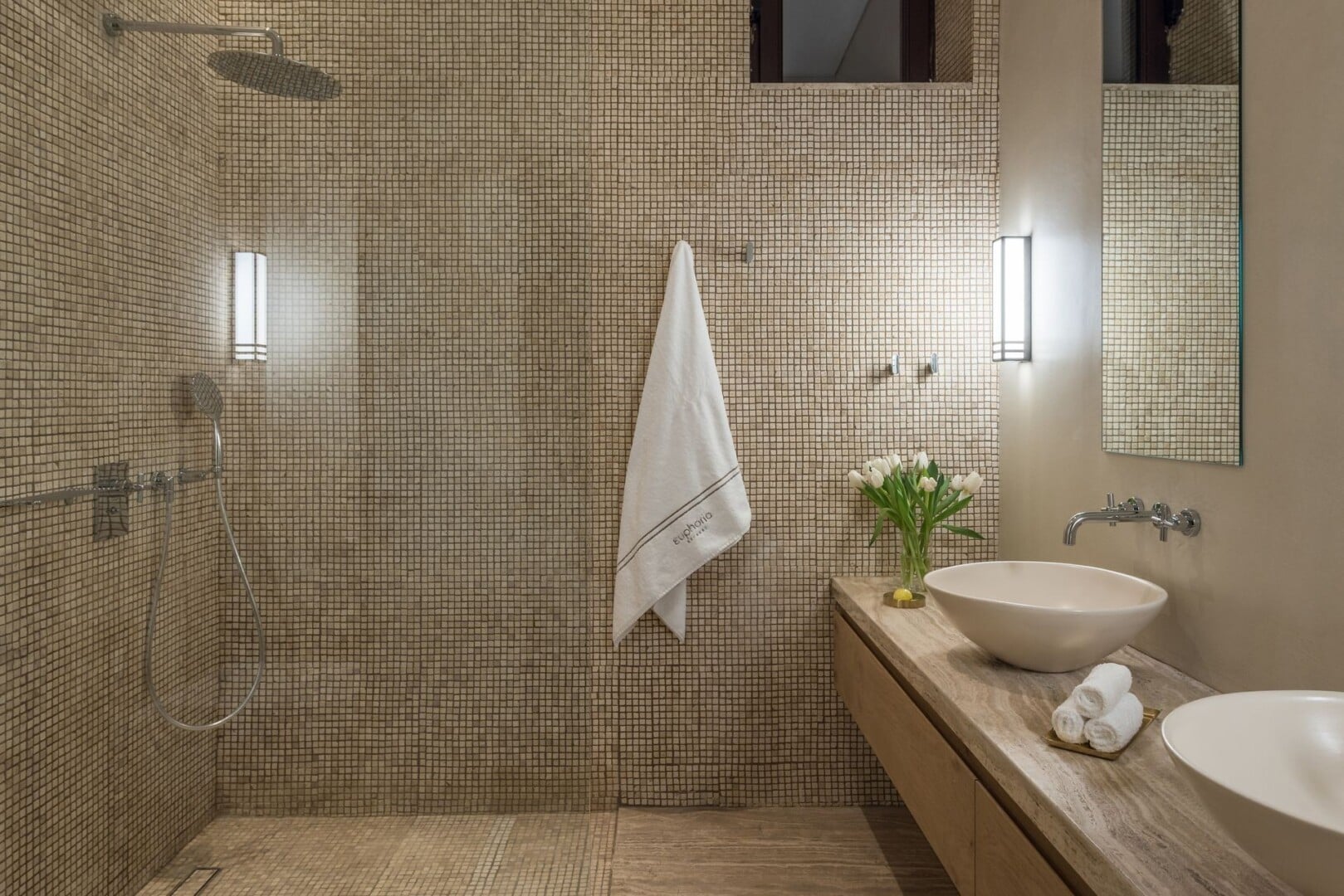Bathroom interior of our Superior Deluxe Room with mosaic tiling in soothing beige tones with two wash basins, featuring a walk-in shower with rain fall and second shower head.