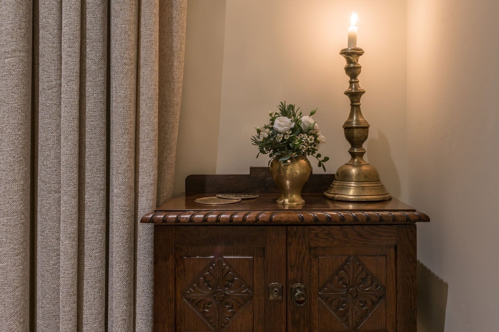 Details of an engraved wooden cupboard with brass vase and candle holder.