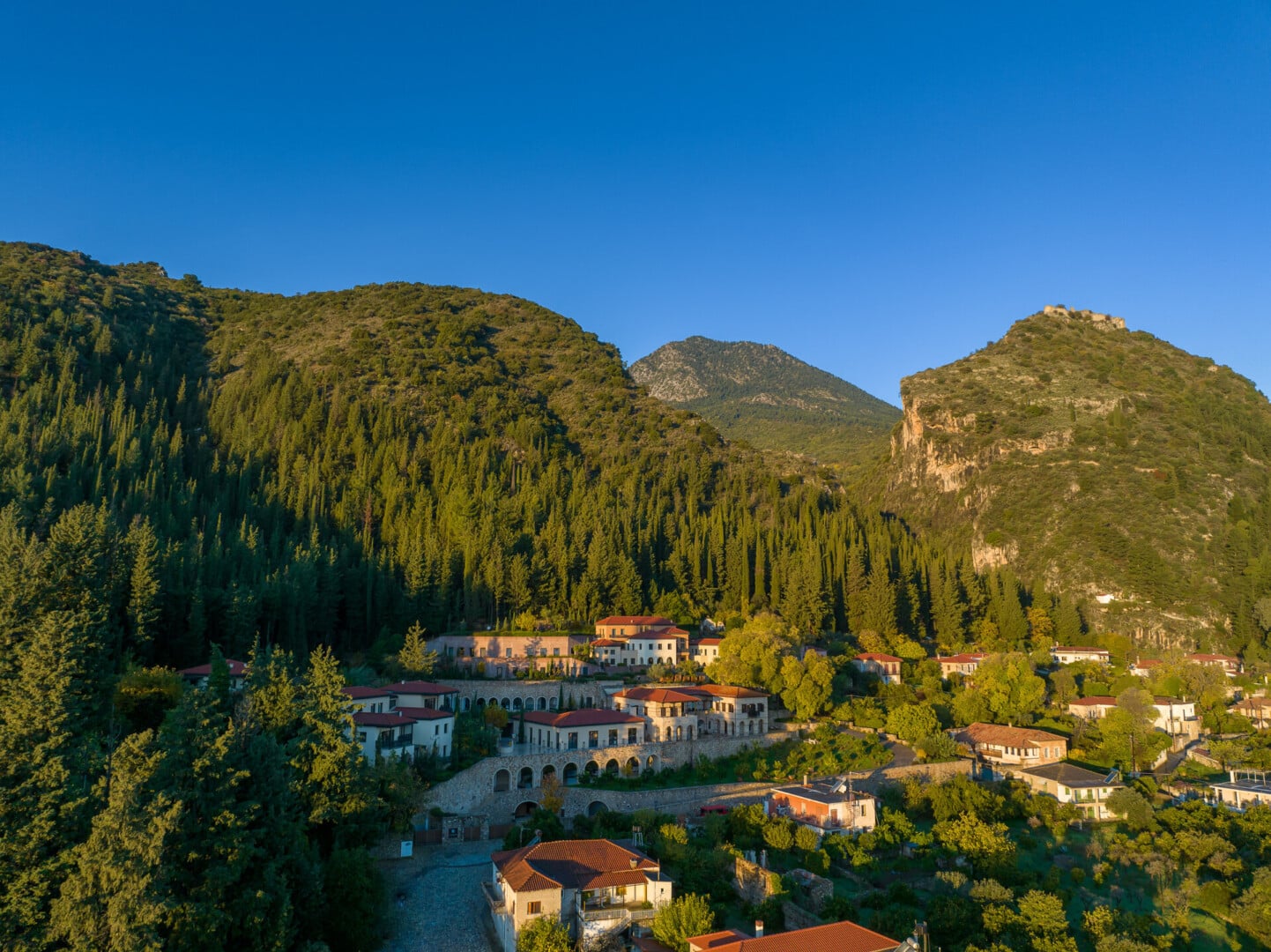The verdant embrace of Euphoria Retreat, amidst the green forest at the foothills of mount Taygetus and the castle of Mystras in the background.