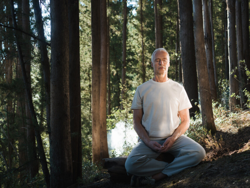 Mature man meditating cross-legged in a pine forest at Euphoria Retreat, best spa for solos in Greece as named by The Times and The Sunday Times